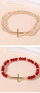 Detail of red and champagne beaded bracelets with golden cross pendants on white stands