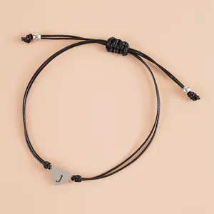 Detail of adjustable black woven bracelet featuring a silver heart charm with letter J