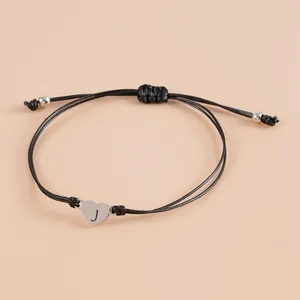 Detail of adjustable black woven bracelet featuring a silver heart charm with engraved letter J
