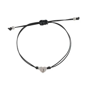 Detailed view of woven black cord bracelet with silver heart pendant engraved letter J