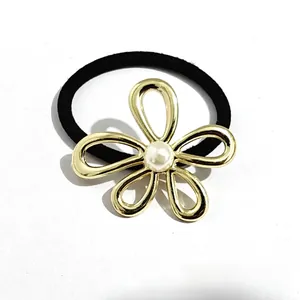Close-up of golden hollow flower hair tie with central pearl on elastic black band