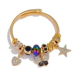 Detail of gold cable bracelet featuring heart arrow, butterfly and star charms with crystals