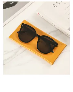 Close-up of black oversized sunglasses with a yellow lychee pattern leather pouch on marble