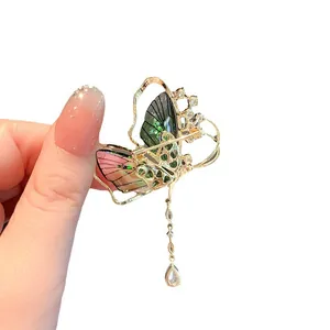 Elegant emerald butterfly brooch with gold trim and crystal tassel on white background