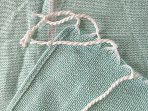 Macro detail of white twisted tassels on a mint green striped Turkish towel.
