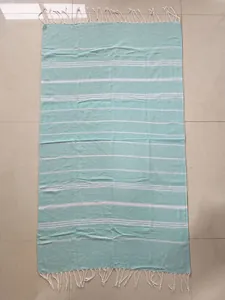 Top-down view of a mint green Turkish beach towel with white stripes and tassels.