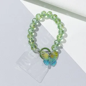 Macro view of iridescent butterfly charm and faceted green beads on a stylish phone wristlet