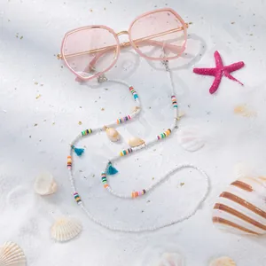 Détail d'une chaîne de lunettes bohème avec perles et coquillages sur plage blanche