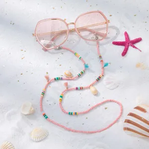 Détail d'une chaîne de lunettes perlée colorée avec coquillages sur sable blanc fin