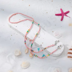 Détail d'une chaîne à lunettes en perles roses avec pompons et coquillages sur sable