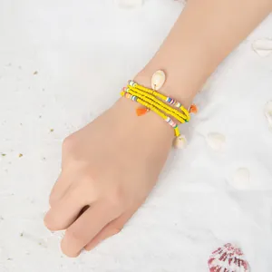 Détail d'un bracelet bohème multicouche avec perles, coquillages et pompons orange vif