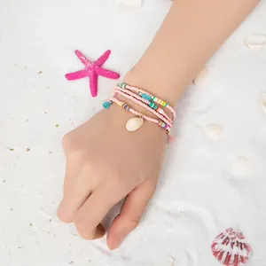 Bracelet multicouche bohème avec perles, coquillages et pompons sur sable blanc