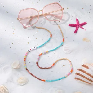 Detail der Brillenlkette mit LOVE-Buchstaben und bunten Perlen auf weißem Strand im Sand