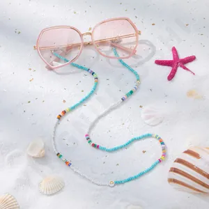 Detail einer Sonnenbrille mit handgefertigter Perlenkette auf sandigem Strandhintergrund