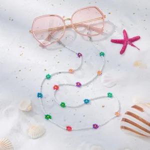 Detailansicht der rosa Sonnenbrille mit bunter Perlen-Blumenkette auf feinem Sand