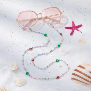 Rosa Oversize-Sonnenbrille mit bunter Blumen-Perlenkette auf weißem Strandsand