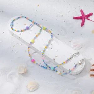 Nahaufnahme der Macaron-Perlenkette mit Herzanhängern auf Muscheln und Sand