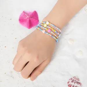 Detail von vier handgefertigten Perlenarmbändern mit Herz in Pastellfarben auf Sand