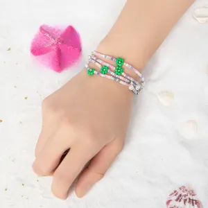 Detail eines Perlenarmbands mit grünen Blumenanhängern und bunten Glasperlen am Handgelenk