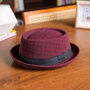 Close-up of burgundy plaid dome hat with black grosgrain band on a wooden desk