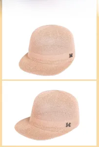 Detail of pink straw equestrian hat featuring a metallic M logo and fine woven texture
