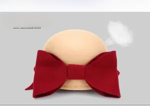 Close-up of beige wool equestrian hat featuring a large red bow and breathable fabric