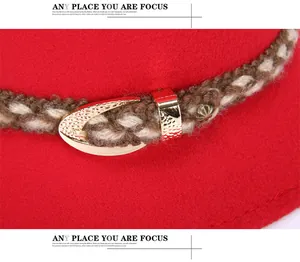 Dettaglio di un cappello in feltro rosso con fascia intrecciata e fibbia in metallo oro