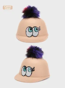 Close-up of children's camel wool felt hat featuring sequin eyes and a colorful fur pompom