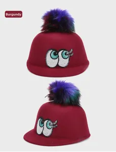 Detail of wine red felt hat featuring vibrant faux fur pompom and sequined eye design