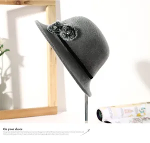 Side view detail of a grey winter wool cloche hat with fur pom-poms and black ribbon.