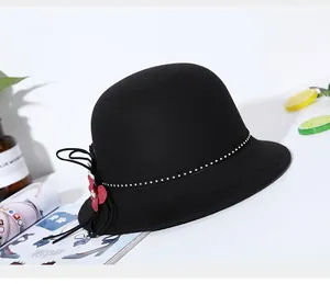 Detail of black wool felt hat featuring red flower accent and polka dot ribbon trim