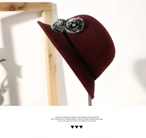 Detail of burgundy wool bucket hat with decorative fur pompoms and rhinestones
