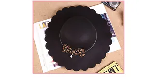 Detail of black wool fedora with wavy brim featuring leopard bow and pearl charm
