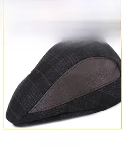 Close-up of men's winter cap showing grey plaid fabric and brown leather stitching detail