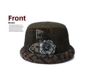 Front view of a brown winter cloche hat with thick fabric, faux fur pom and leaf details