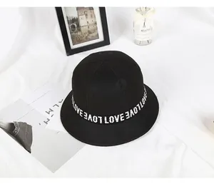 Detail view of black felt bucket hat featuring white LOVE letter ribbon on a white fabric