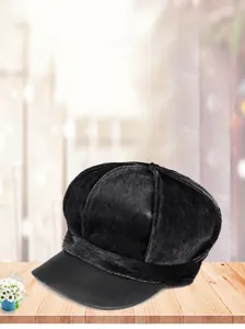 Close-up of black faux fur newsboy cap with a stylish leather brim on wooden surface