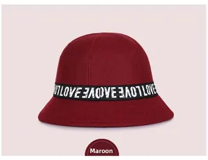 Detail of burgundy wool bucket hat featuring decorative woven ribbon with letter pattern