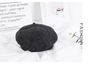Detailed texture of dark grey wool beret on minimalist white fabric with fashion magazine