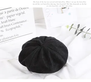Close-up of a black wool beret with a top stalk on white fabric with a prop bag