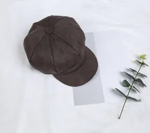 Detailed texture of dark brown suede newsboy cap featuring eight-panel stitching and top button