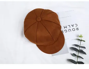 Top view of a brown suede octagonal newsboy cap styled with green leaves and magazines