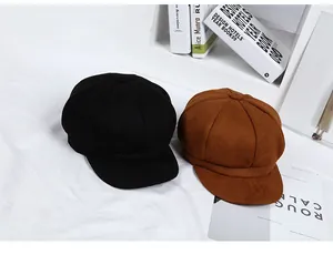 Flat lay of black and brown octagonal newsboy hats on textured white fabric background