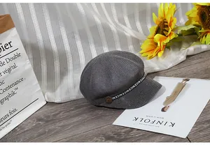 Dettaglio del cappello newsboy in maglia grigia con nastro NICENICE e bottone vintage