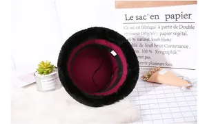 Detail of plush black faux fur bucket hat with warm burgundy lining and adjustable strap