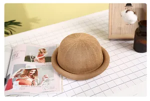 Detail of a brown woven straw hat featuring a rounded crown and elegant rolled brim design