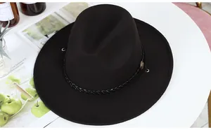 Detail of black wool fedora hat featuring a woven leather band and vintage metal badge