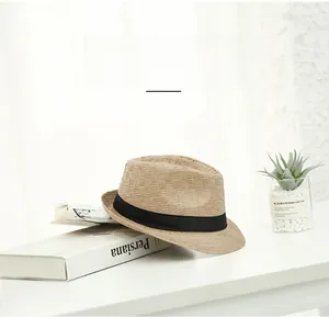 Detailed close-up of a light brown woven straw fedora hat on a white desk with props