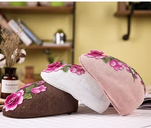 Detailed embroidery of floral patterns on woven berets in brown, white, and pink tones
