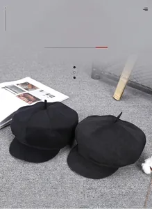 Detail view of two classic black cashmere newsboy hats on a textured grey background
